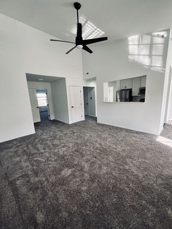 an empty living room with carpet and a ceiling fan